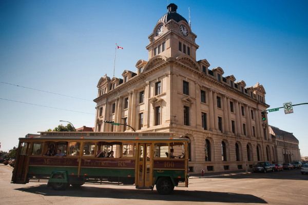 Moose Jaw trolly driving past a historical building during the day in summer
